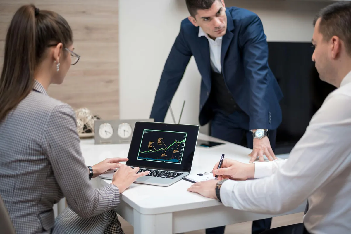 Three colleagues at an office table reviewing a chart on a laptop