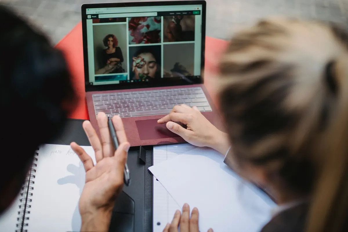 Two people at a table looking over website examples on a laptop, one gesturing as she talks